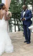 Bride in a white gown faces groom in a blue suit during an outdoor wedding ceremony