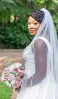 Bride in white veil holding pink bouquet outdoors, smiling over her shoulder