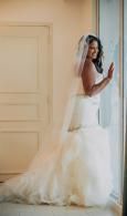 Bride in a white wedding gown standing by a window in a softly lit room