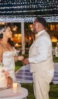 Bride and groom face each other at an outdoor candlelit wedding reception under string lights.