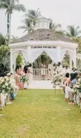Outdoor wedding gazebo aisle with white drapes, flowers, and guests seated on both sides