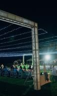Outdoor night event under string lights with people seated and a bright stage light in the background