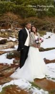 Bride and groom stand together outdoors in a snowy rocky landscape, holding flowers.