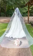 Long white bridal veil draped over a pathway with a bouquet at the base, in an outdoor garden setting
