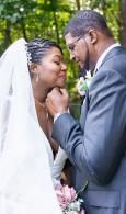 Bride and groom sharing a tender moment outdoors, smiling with flowers in the background