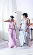 Two people in pastel dresses pose in a bright white studio with flowing fabric.