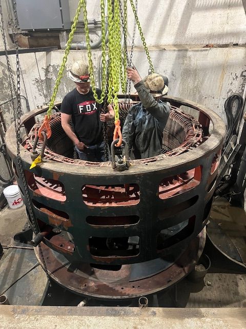 Two workers inside large machinery, using chains to lift a red and black component.