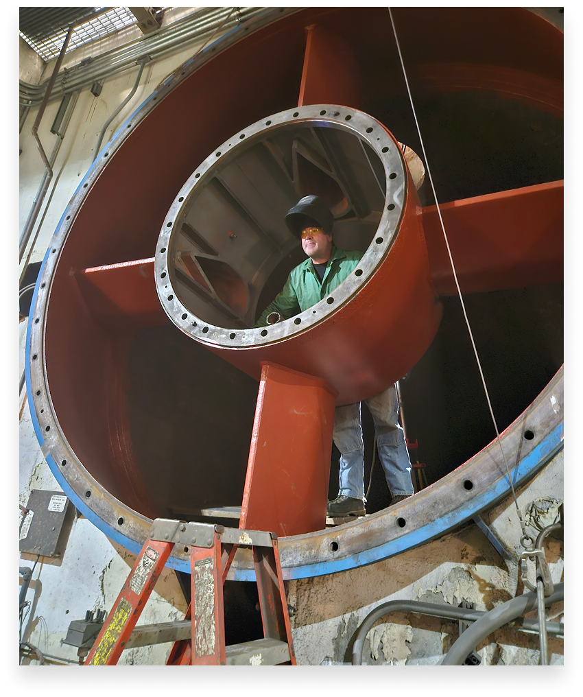 Welder working on a large red industrial turbine component. Wearing a mask and standing inside the structure.