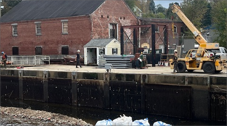 A yellow crane and construction workers at a historic brick building near a canal lock.
