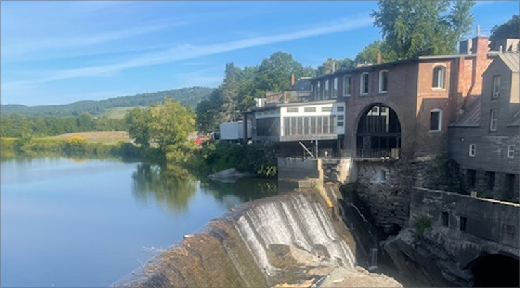 Dam with a brick building, river, and blue sky.