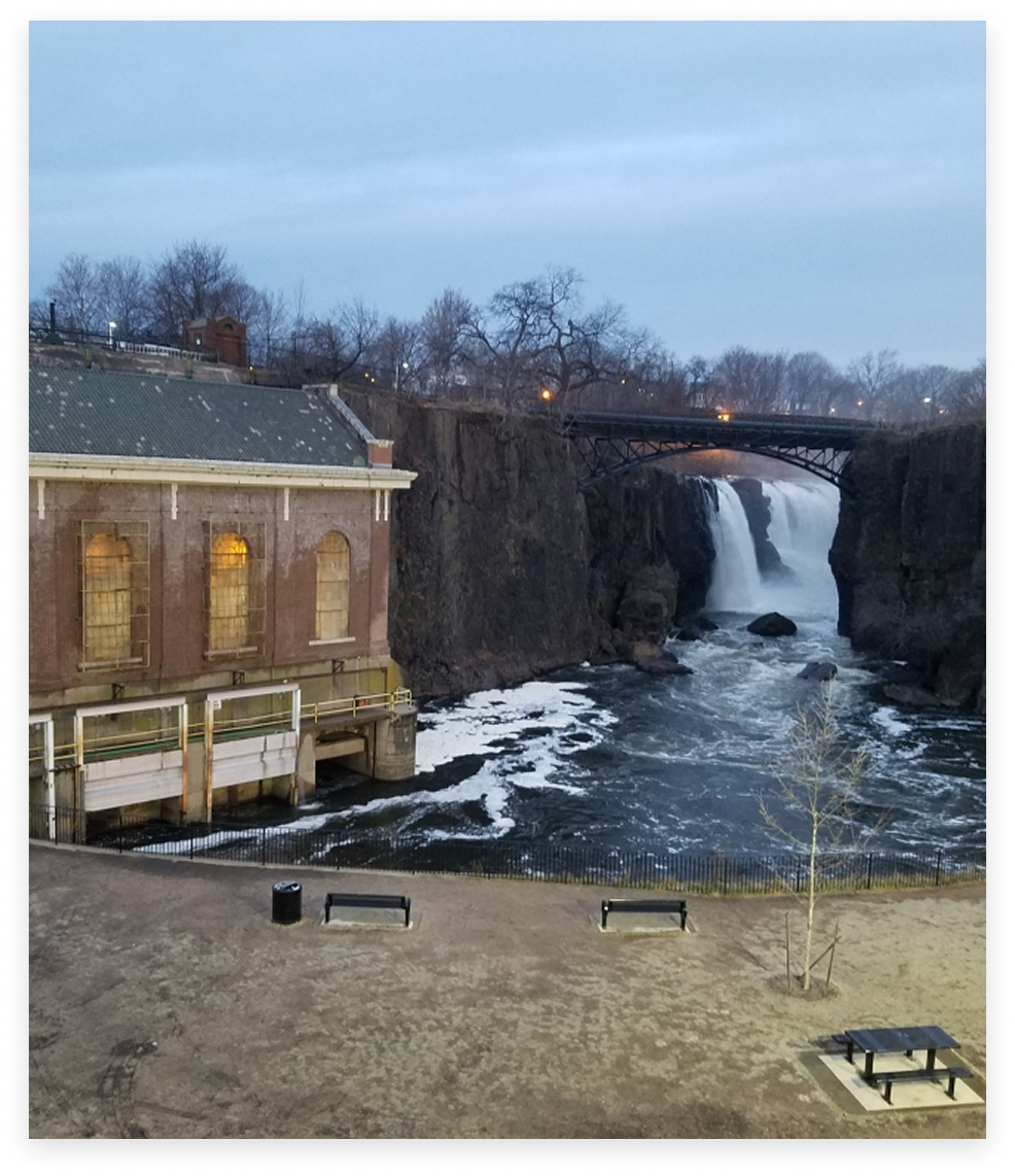 Waterfall cascades over a cliff next to a brick building under a cloudy sky.