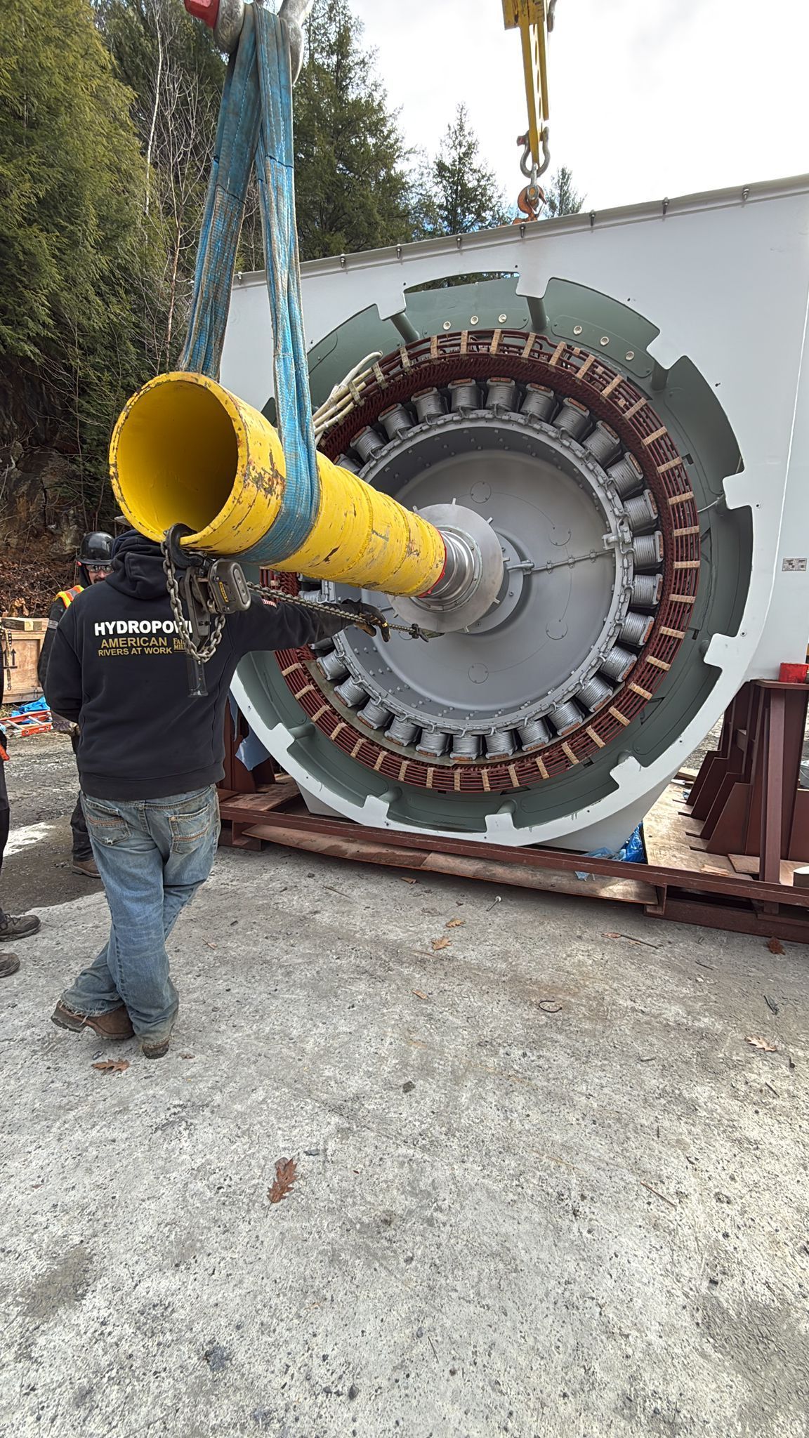 Man with yellow funnel near large industrial motor, being lifted by a crane.