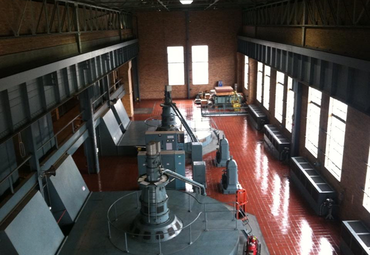 Interior of a power plant with industrial equipment, a red floor, and windows.