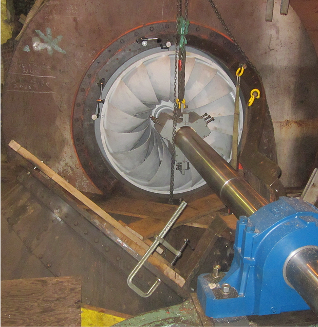 Turbine with blades and a shaft being worked on, suspended by chains. Industrial setting, blue bearing.
