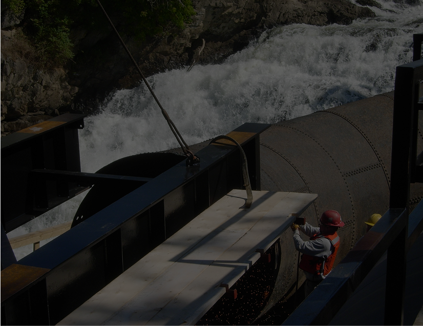A worker in a safety vest adjusts a panel near a fast-flowing waterfall.