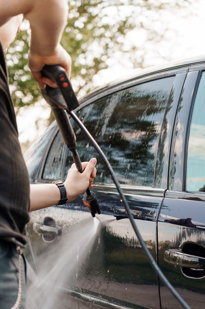 Person washing a black car with a pressure washer outdoors