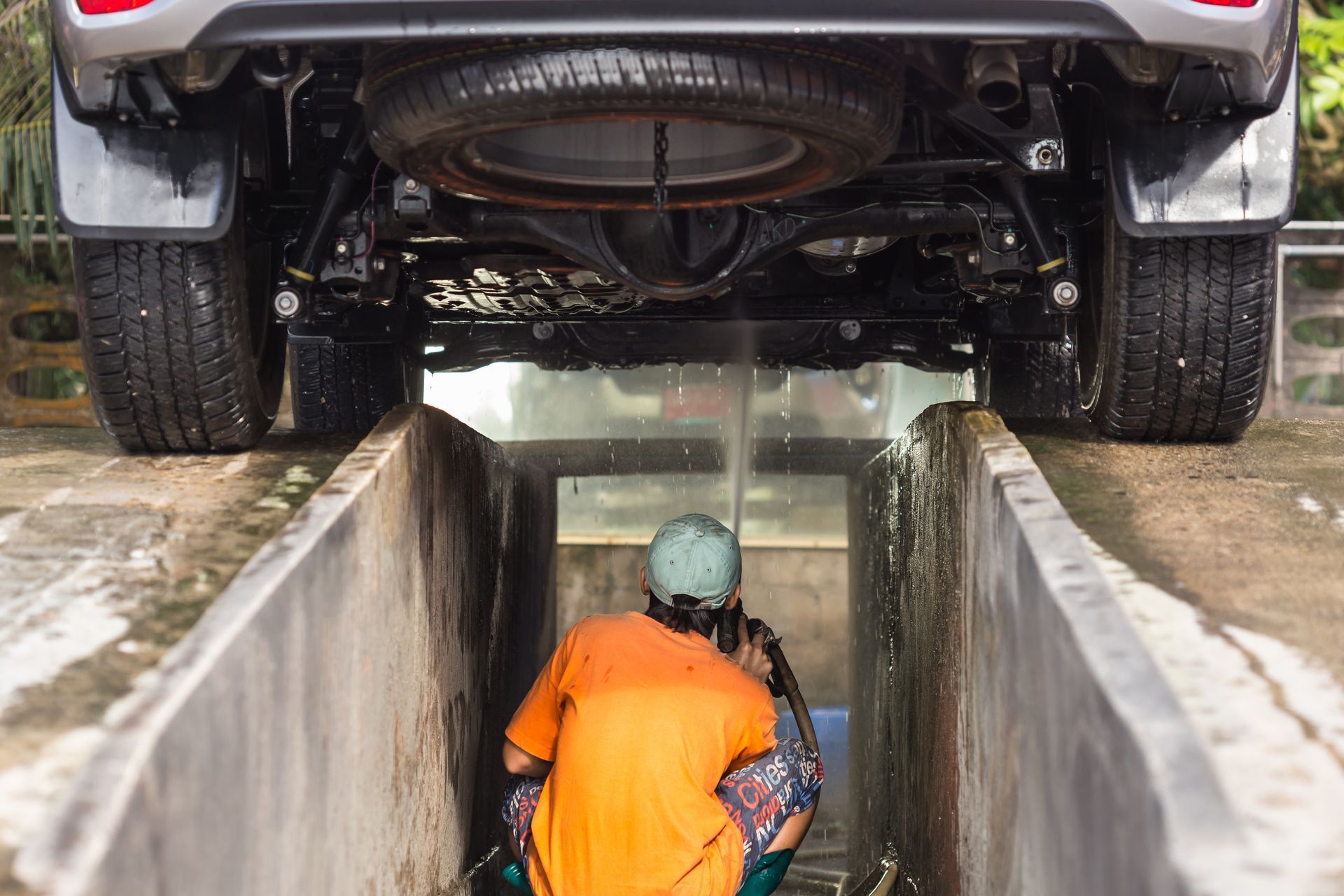 Worker in orange shirt cleaning the underside of a car over a service pit