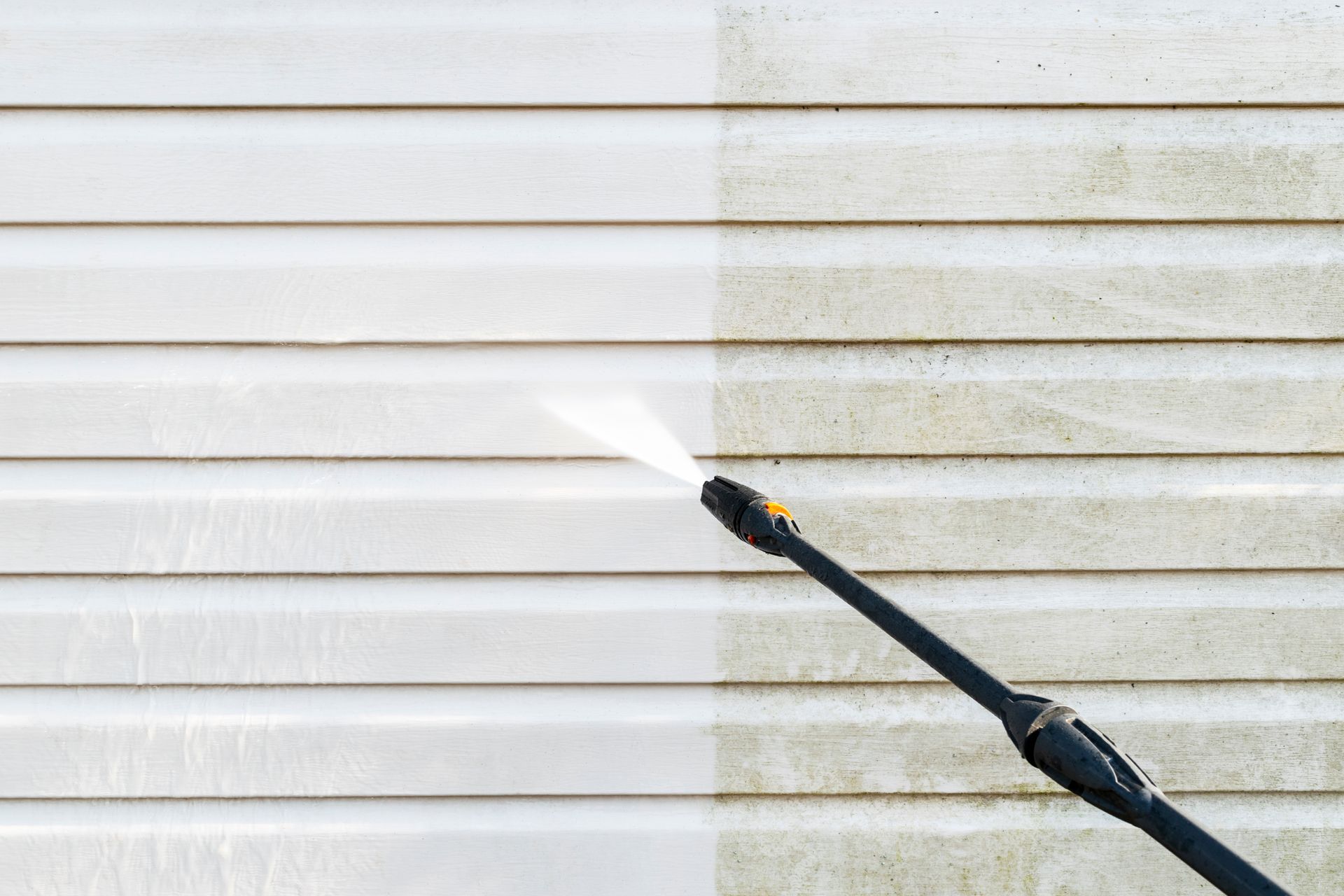 Pressure washer spraying white siding, cleaning a dirty wall with a visible before-and-after contrast