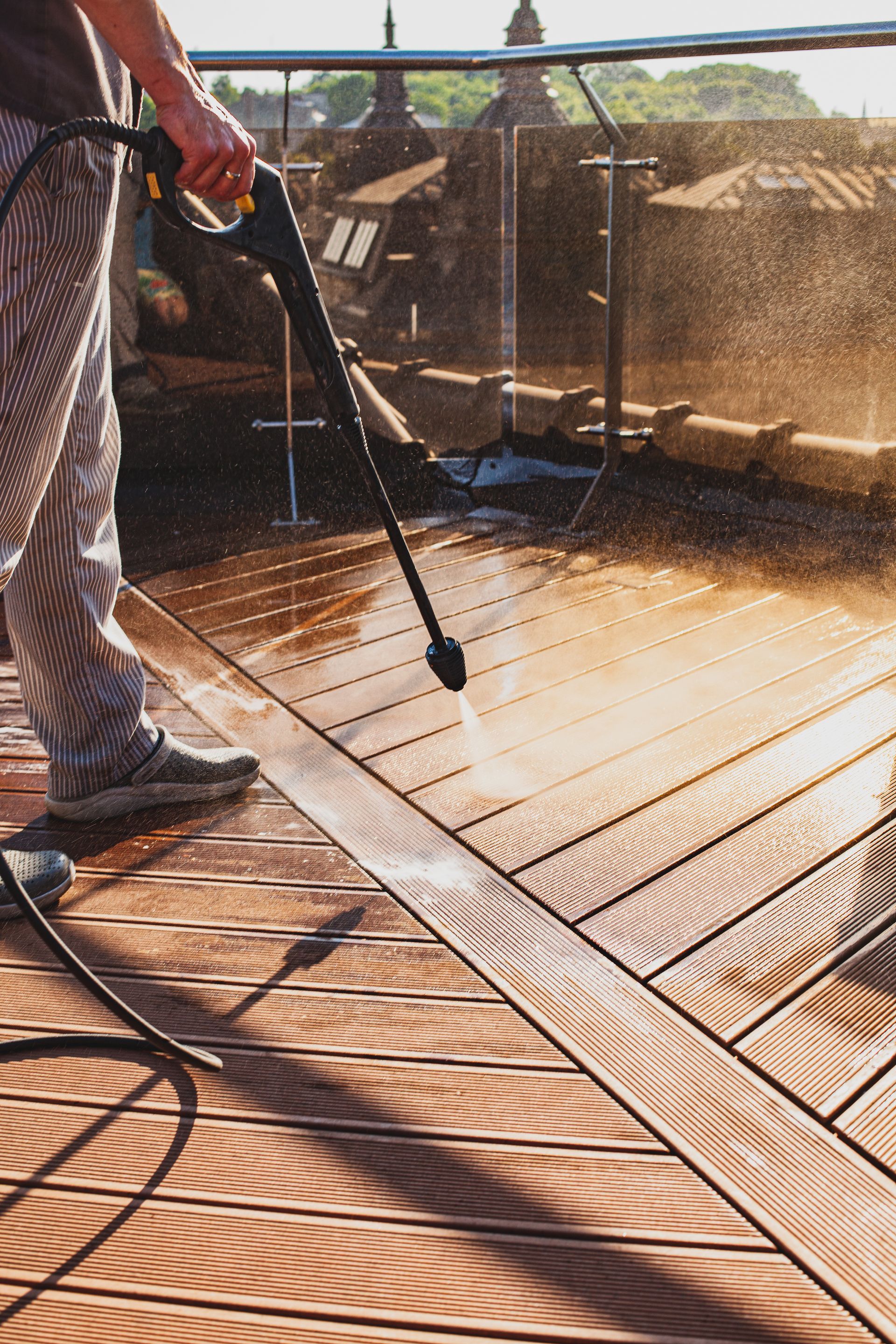 Person pressure-washing a wooden deck in sunlight