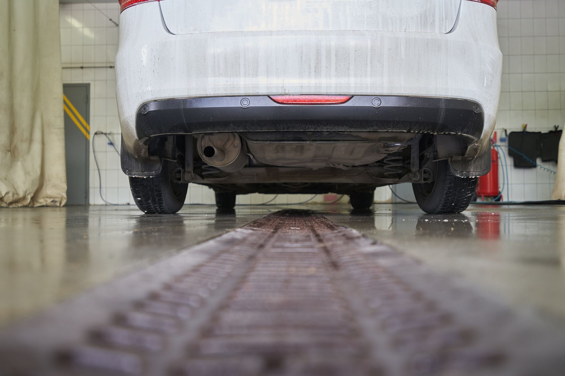 Low-angle view of a white car on a wet workshop floor over a central drainage grate