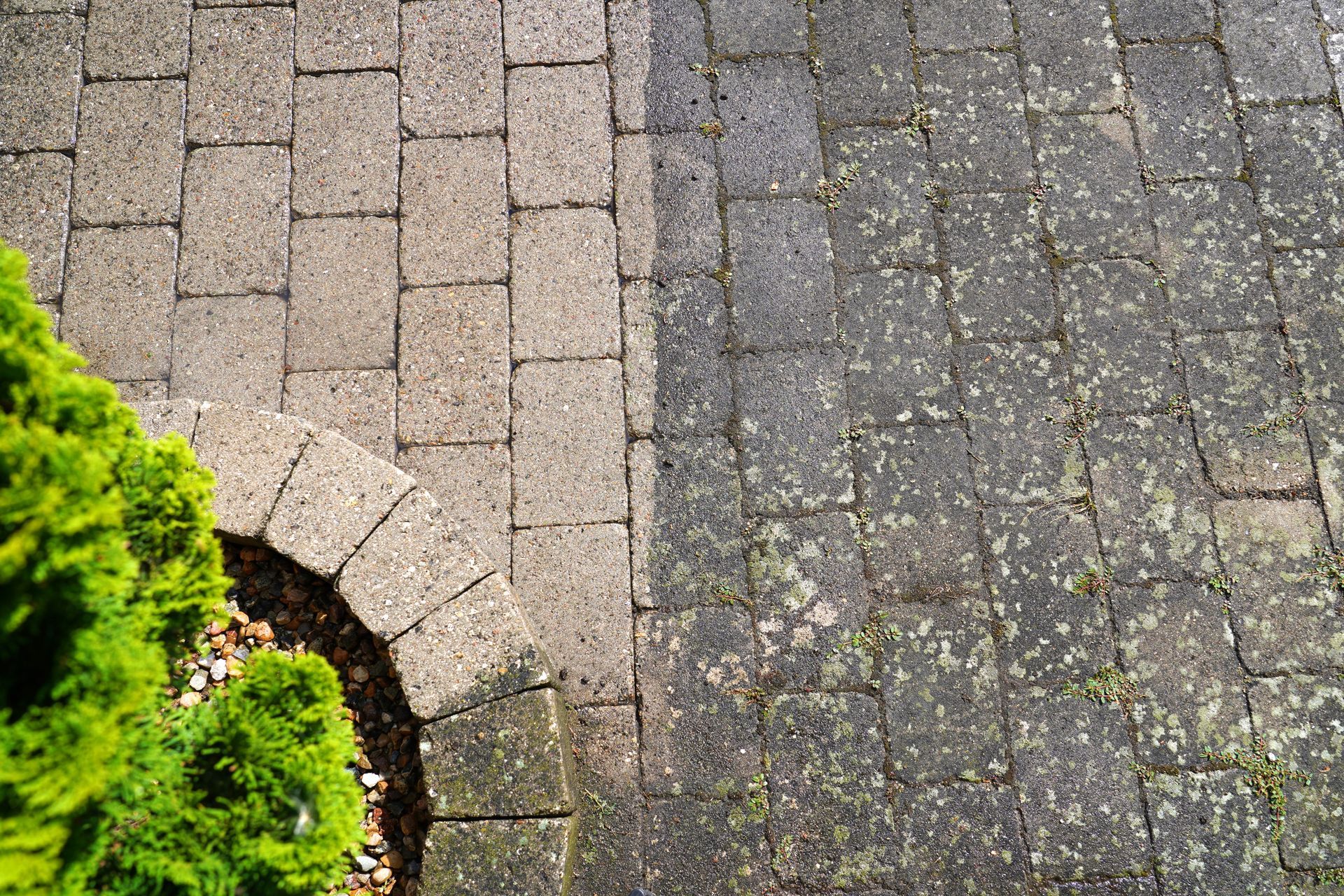 Stone paver path with a curved border beside a dark gravel driveway and green shrubbery.