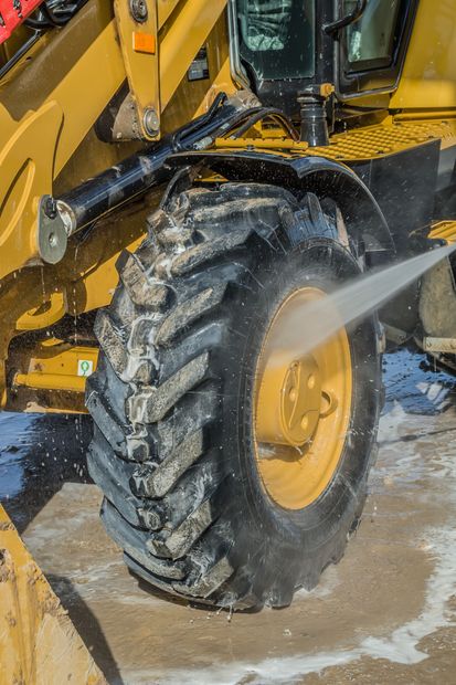 Yellow construction loader tire being sprayed clean with water, muddy ground visible.