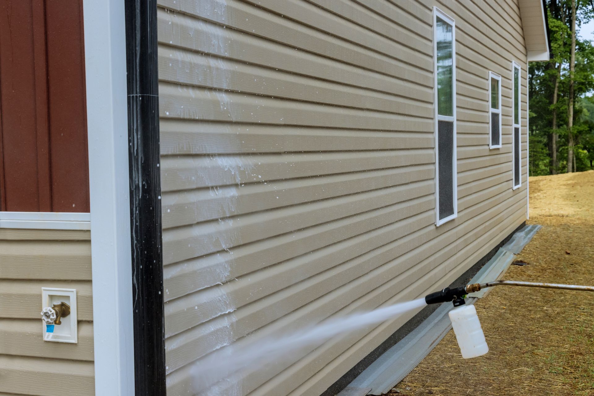 House siding with a white drain pipe and utility access box beside a gravel yard.