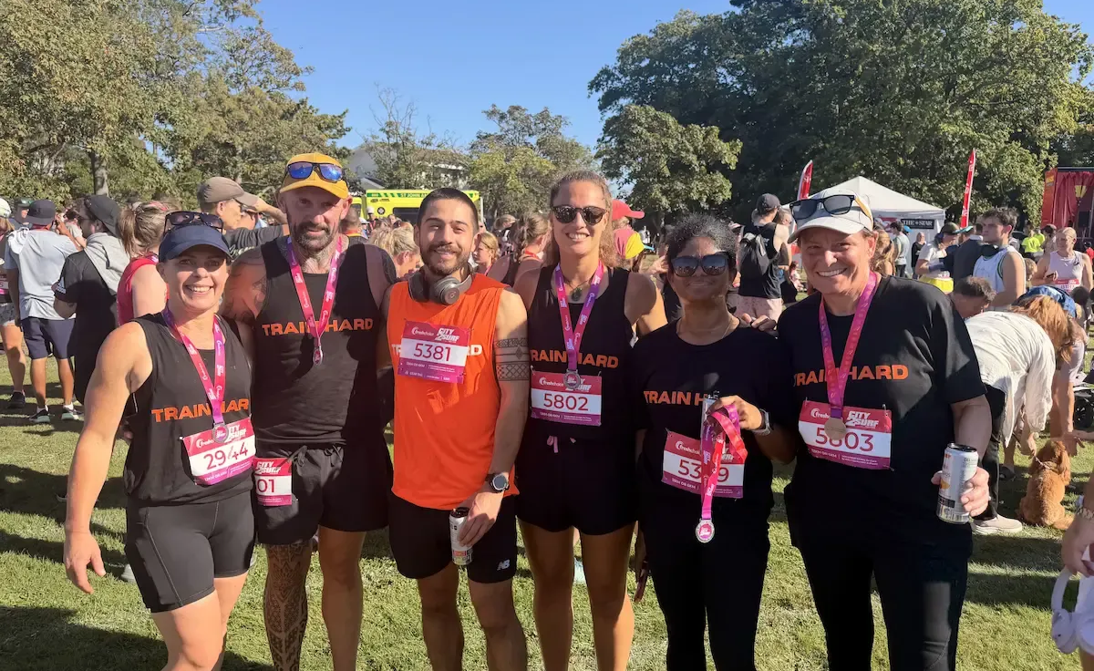 Man boxing a heavy bag in a gym, wearing gloves and smiling while throwing a punch.