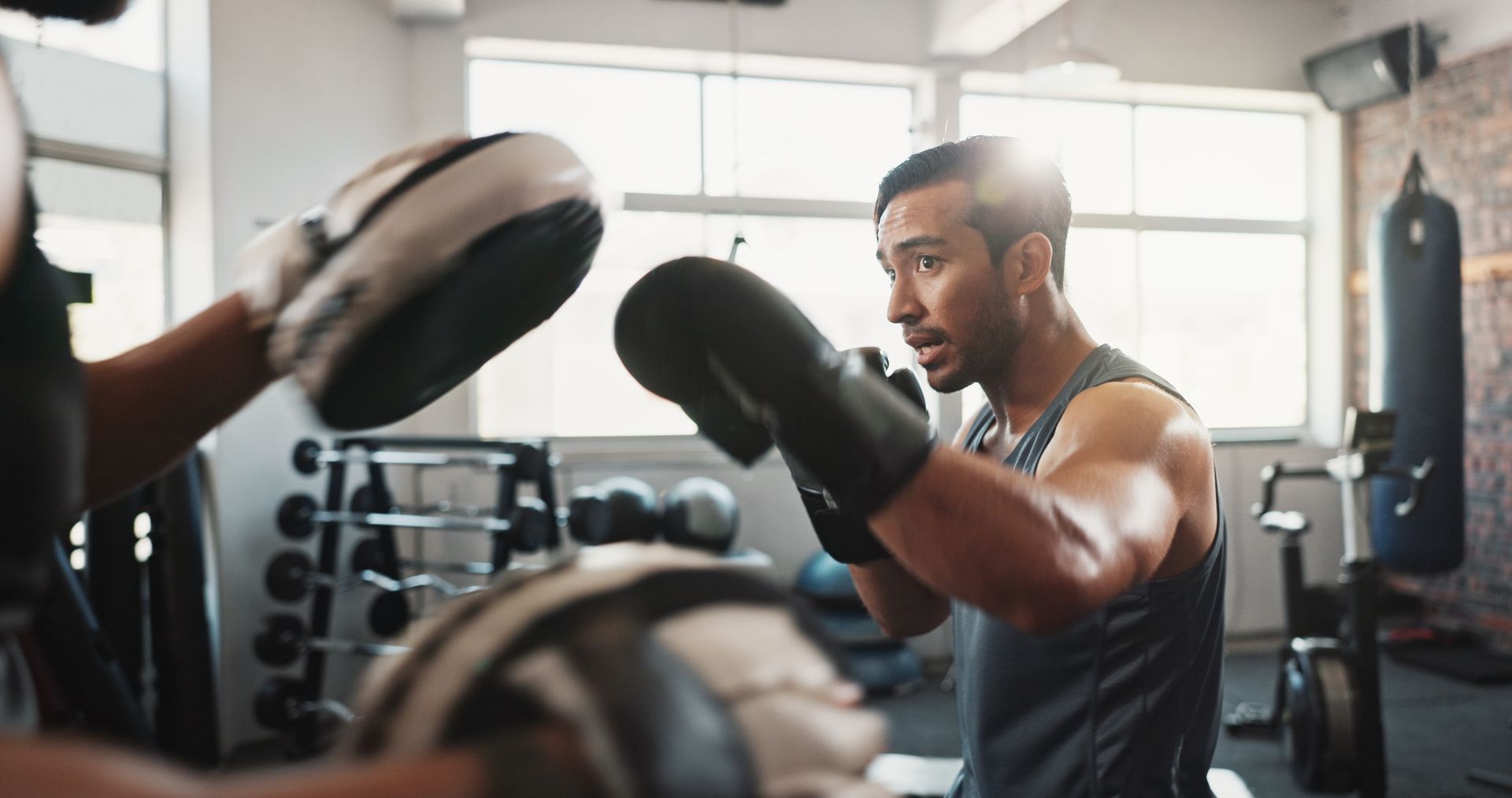 Boxer in black gloves practices punches with a trainer in a gym.