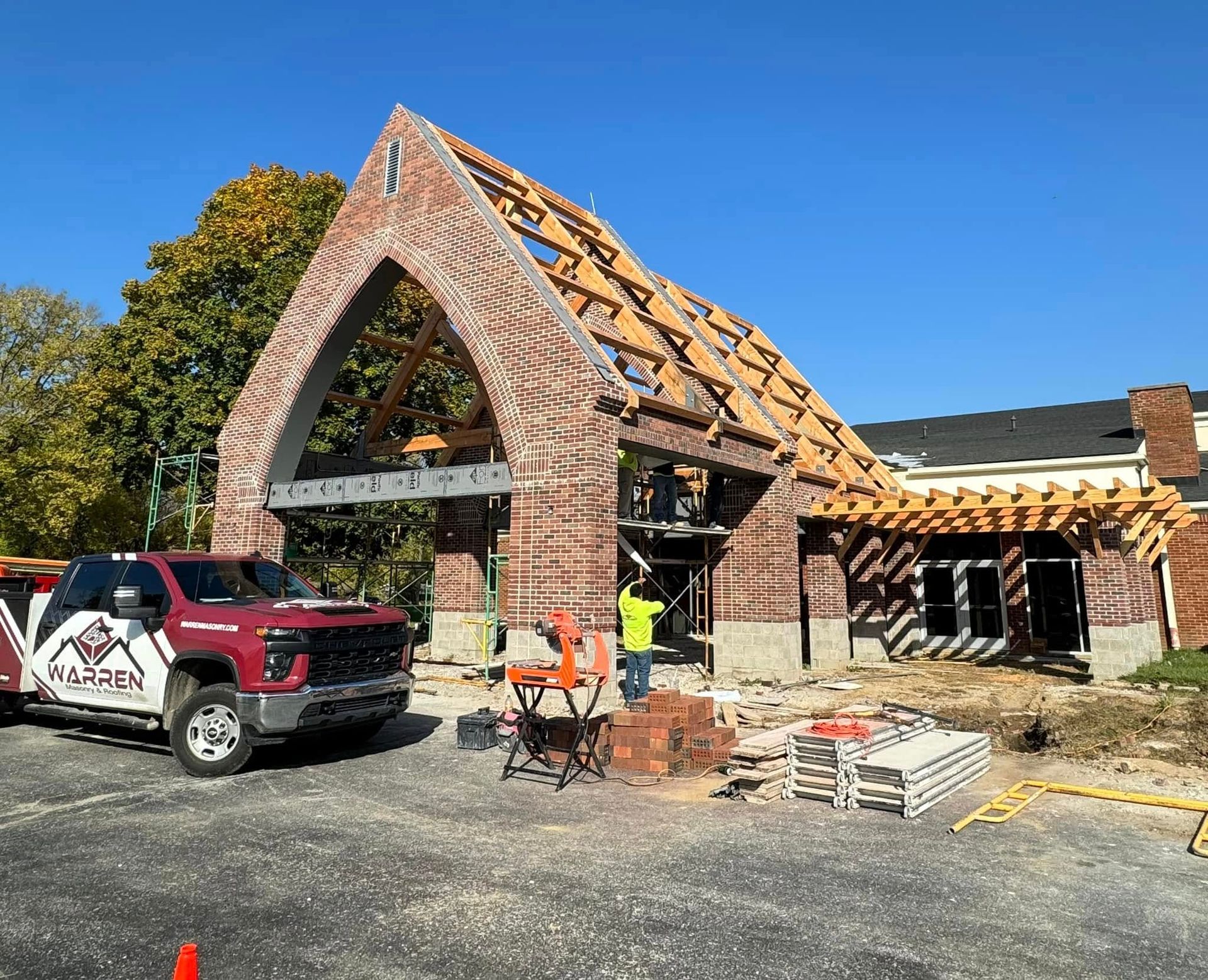 A red pickup truck is parked in front of a brick building under construction with exposed wooden roof framing.