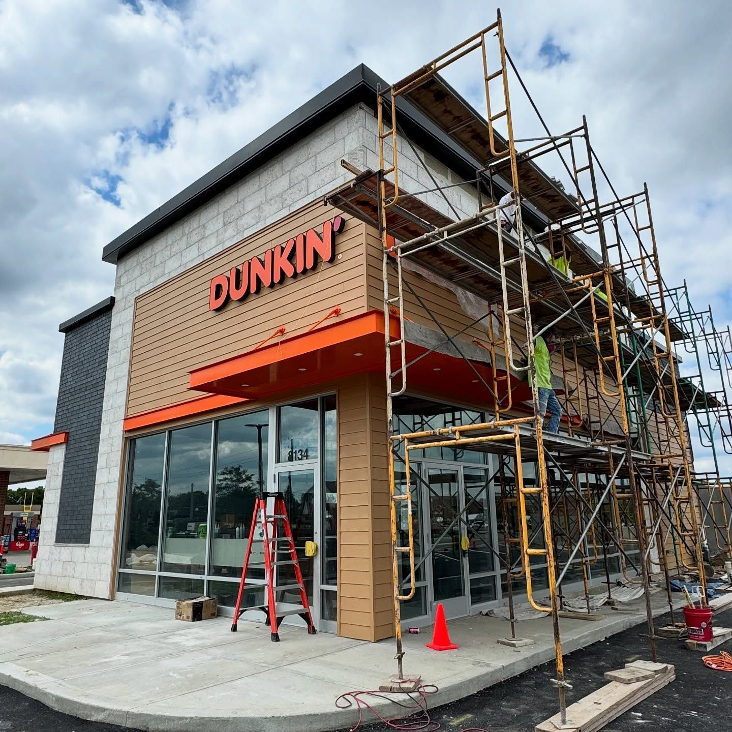 A newly constructed Dunkin' building under renovation with orange trim, light-colored siding, and metal scaffolding.