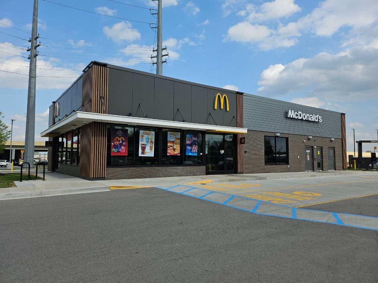 A modern McDonald's restaurant with a gray exterior, wood-accented corner, and bright blue parking lot markings.