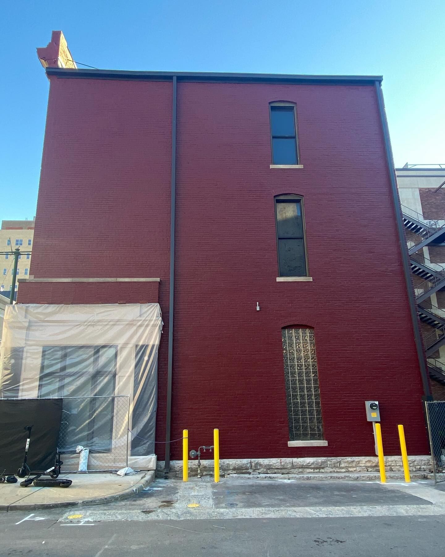 A multi-story maroon brick building with three windows, a glass-block section, and yellow bollards on a city street.