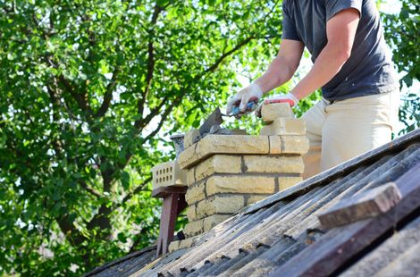 A person wearing work gloves repairs a brick chimney i