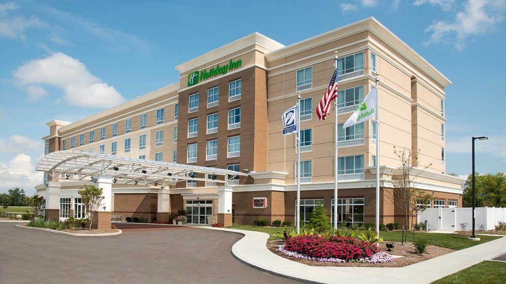 A modern, multi-story Holiday Inn hotel building under a clear blue sky with flags flying in front of the main entrance.