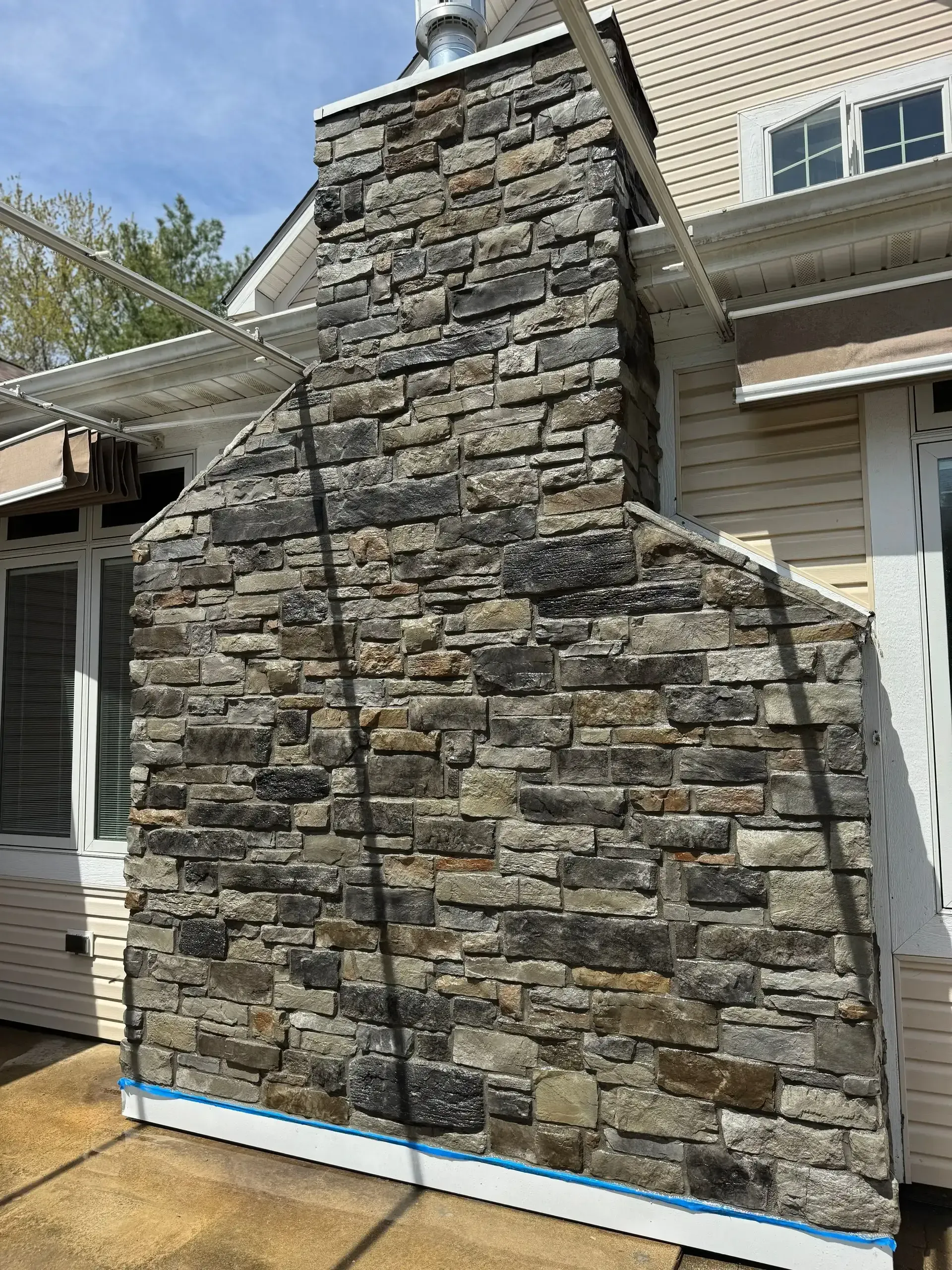 Stone chimney facade on a house exterior with blue trim and construction wrap at the base