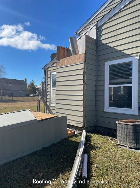 Exterior view of a residential house with a damaged chimney structure and loose siding near a fallen gutter.