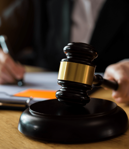 Gavel on wooden block; person in suit writing in background.