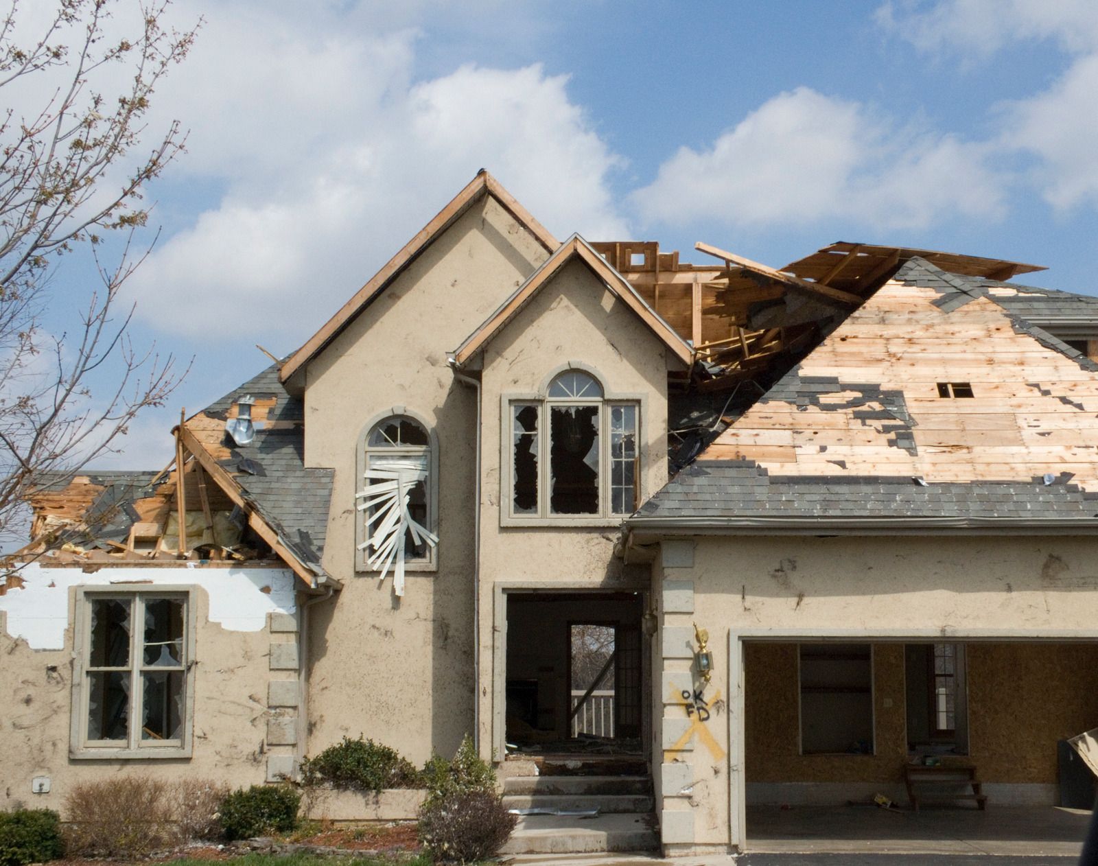 House damaged by severe weather with missing roof and shattered windows.