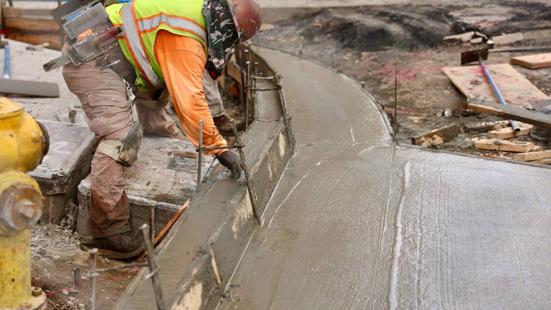A construction worker is pouring concrete on a sidewalk.