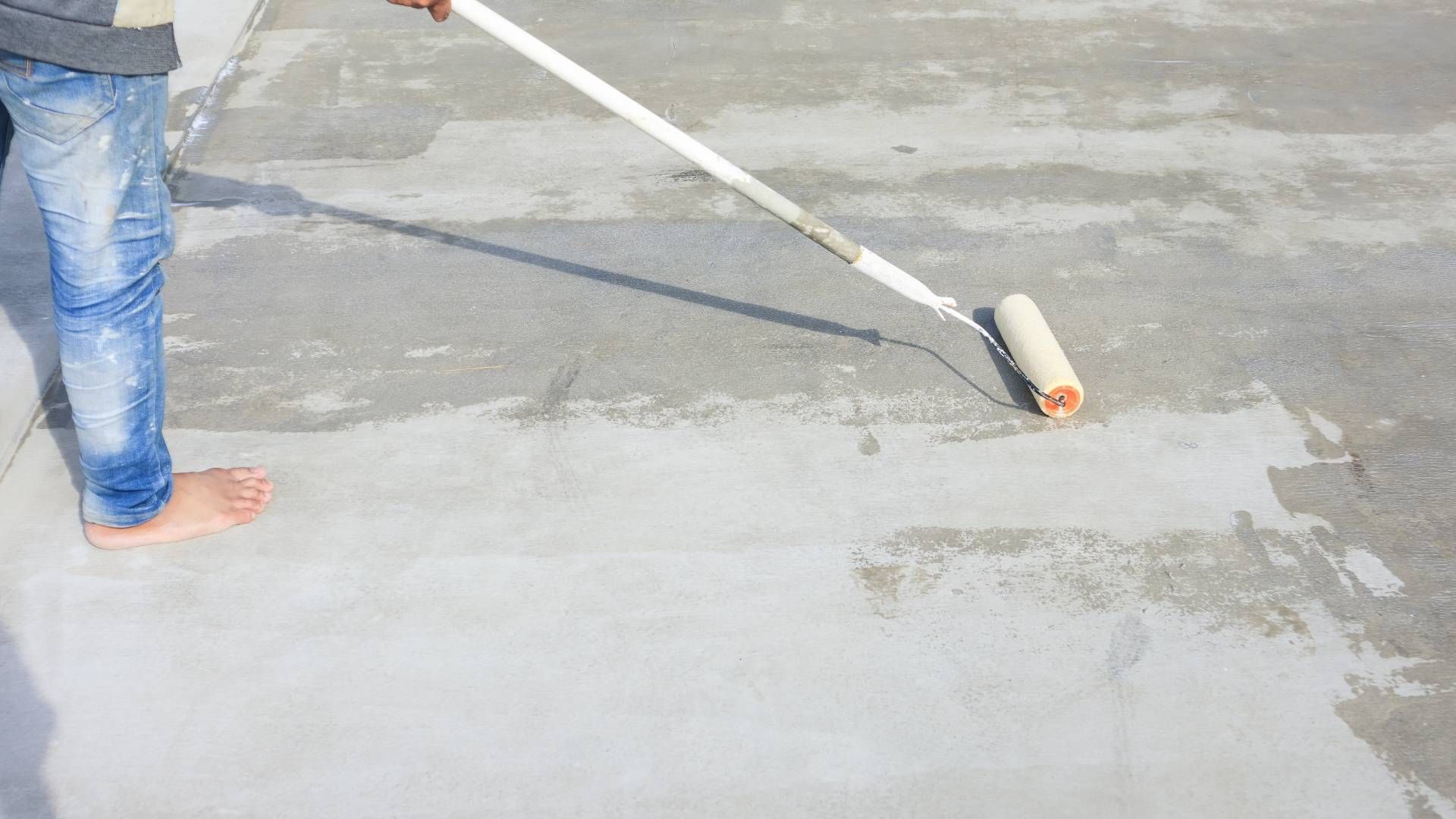 A person is painting a concrete floor with a roller.