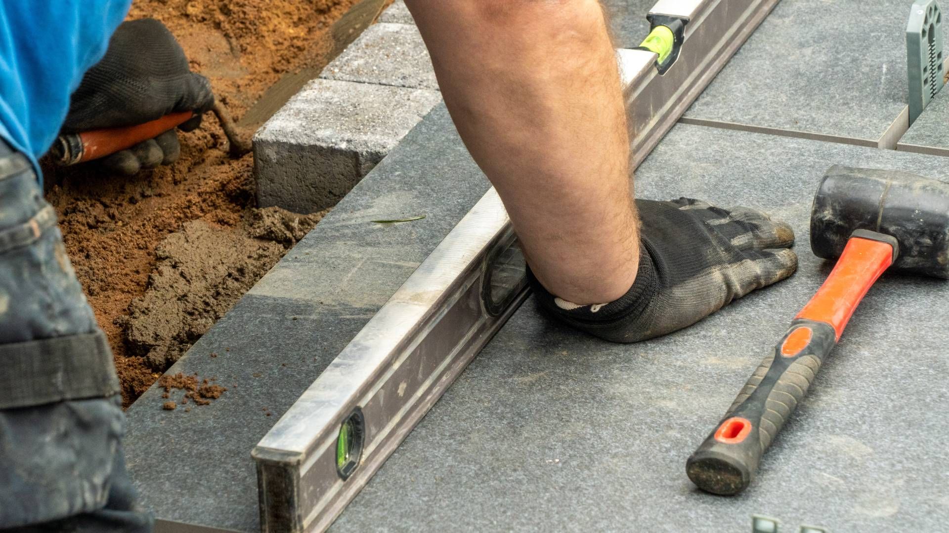 A man is using a level and a hammer to level a brick walkway.