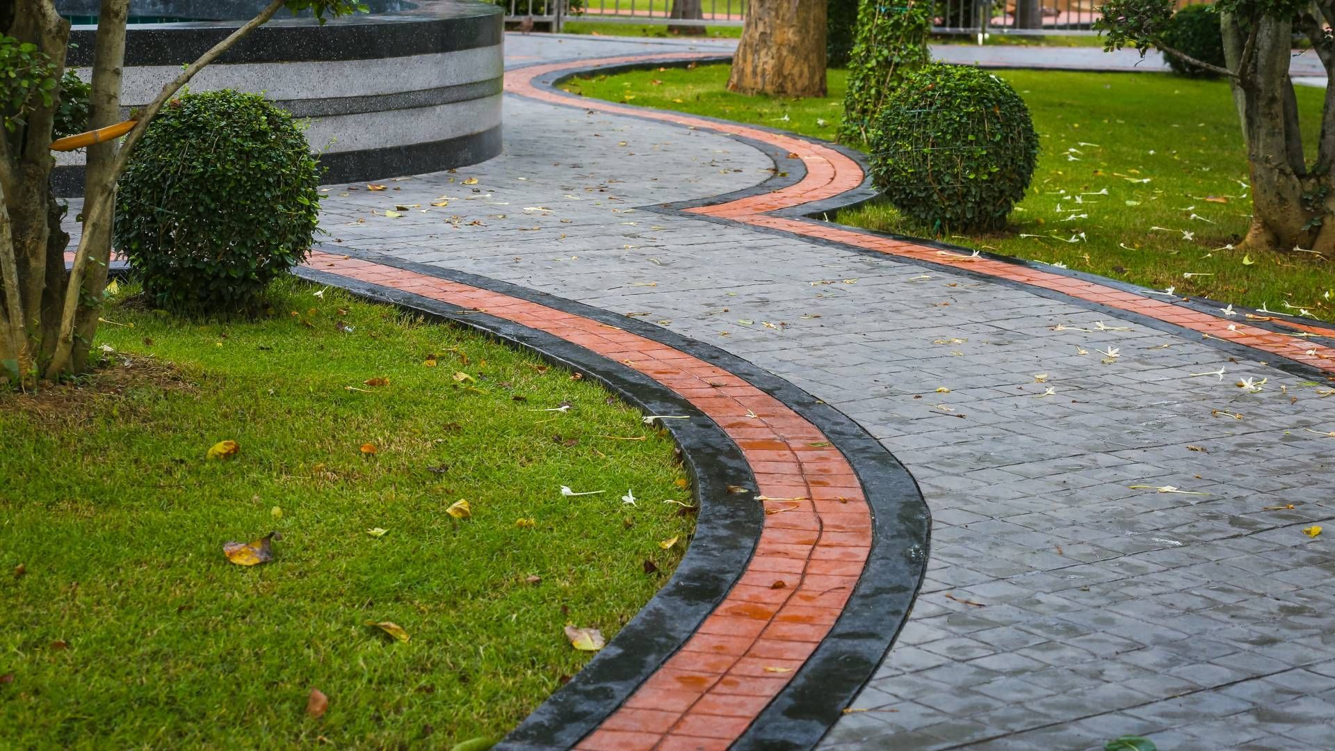 A brick walkway in a park surrounded by grass and trees.