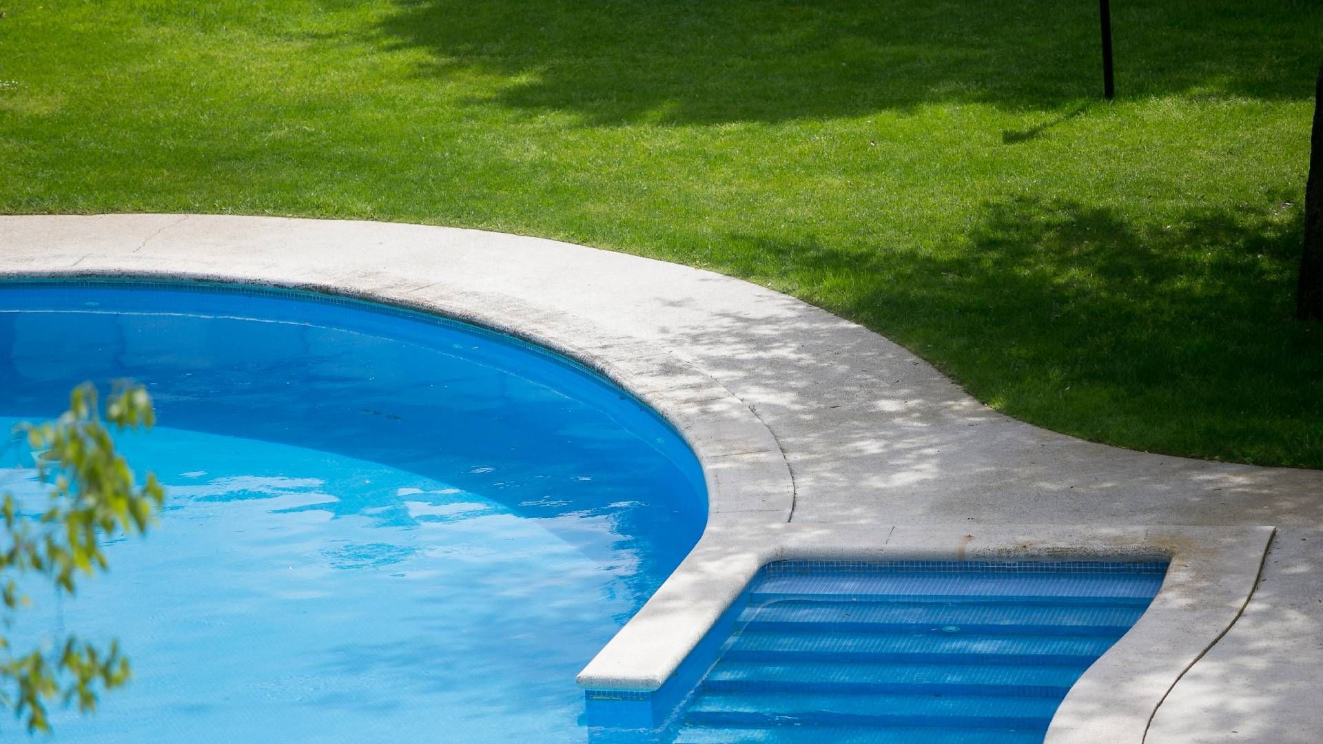 A swimming pool with stairs leading to it and a tree in the background.