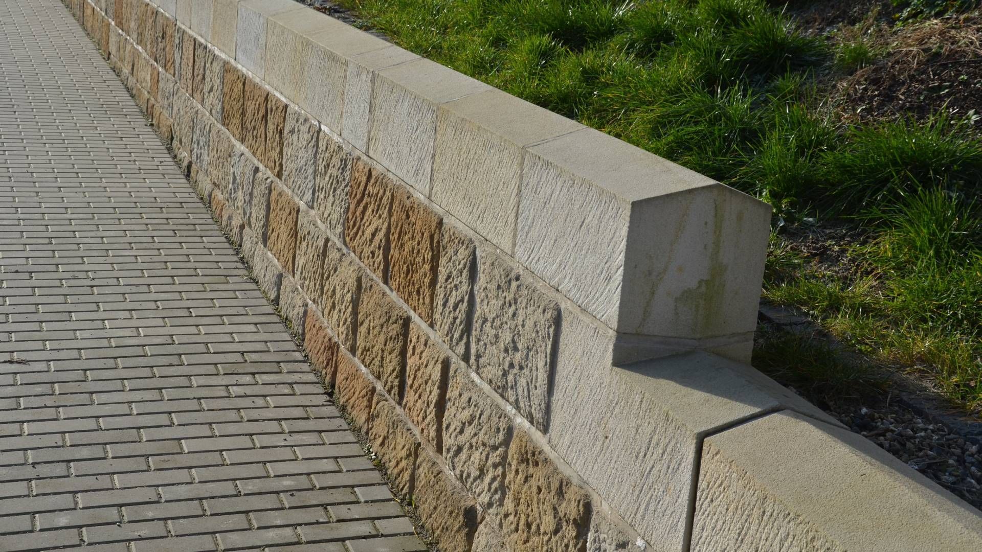 A stone wall along a sidewalk with grass in the background