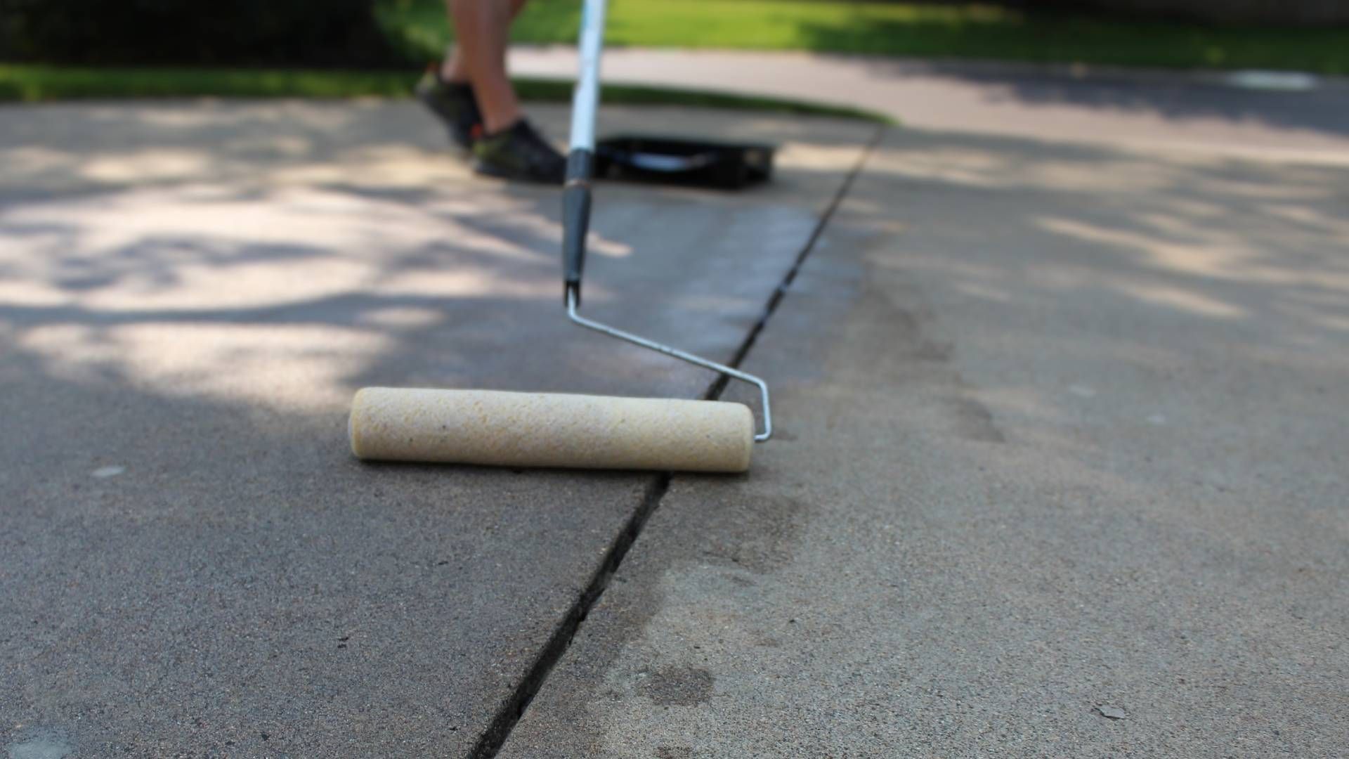 A person is painting a concrete driveway with a roller.