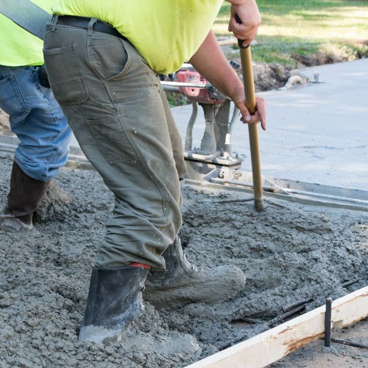 A man in a yellow shirt is working on a concrete driveway