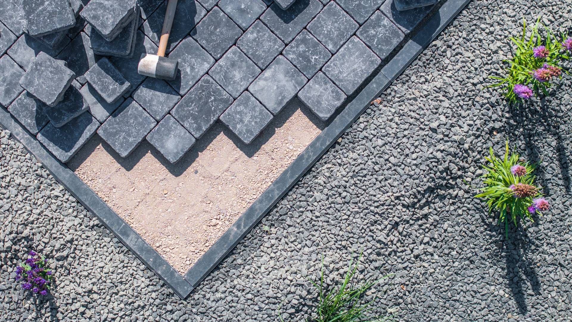 A person is laying bricks on top of gravel in a garden.
