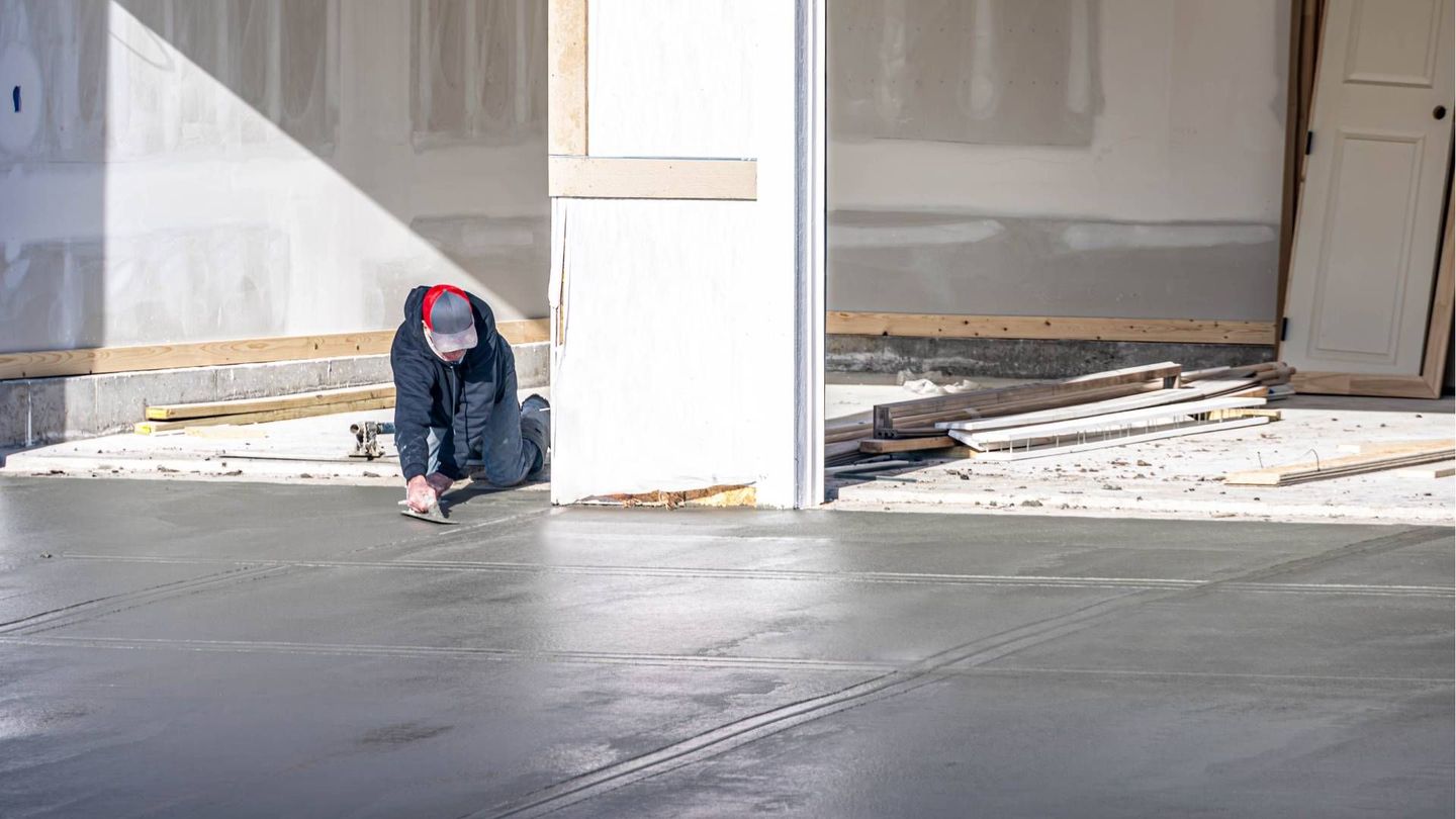 A man is kneeling on the ground working on a concrete driveway.