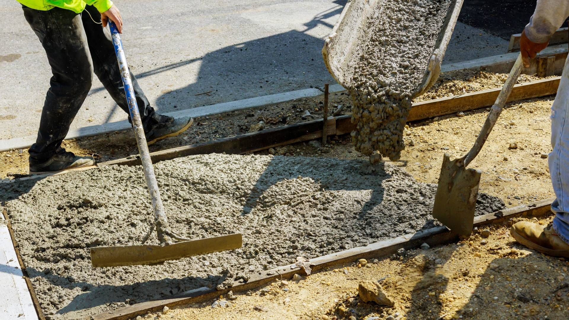 A man is pouring concrete into a concrete slab with a shovel.
